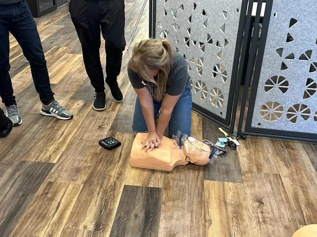 A Skills Training Group learner practising chest compressions with an AED training unit beside the manikin