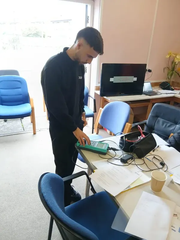 A learner practising with PAT testing equipment at a classroom table